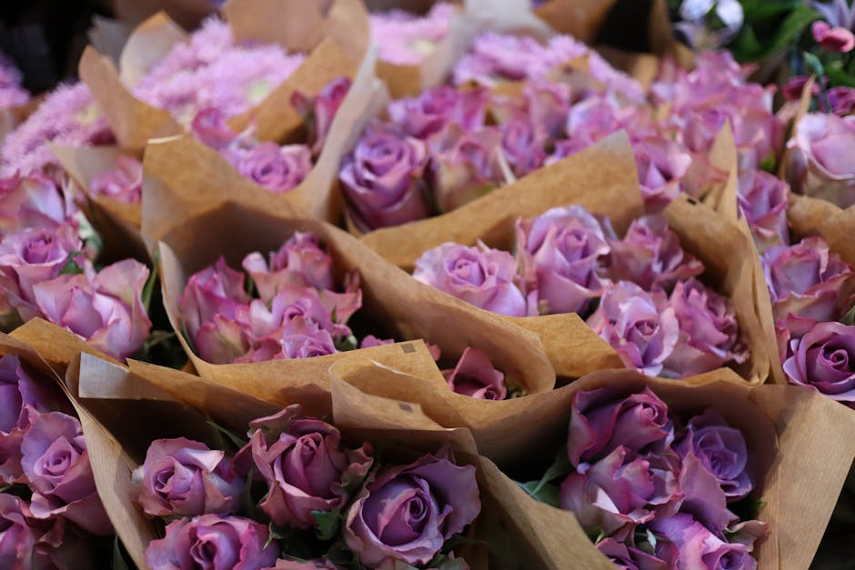 A collection of fresh pink and lavender roses arranged in small bundles wrapping in brown kraft paper, ready for flower delivery or floral gifting. The roses display vibrant petals with a soft, velvet